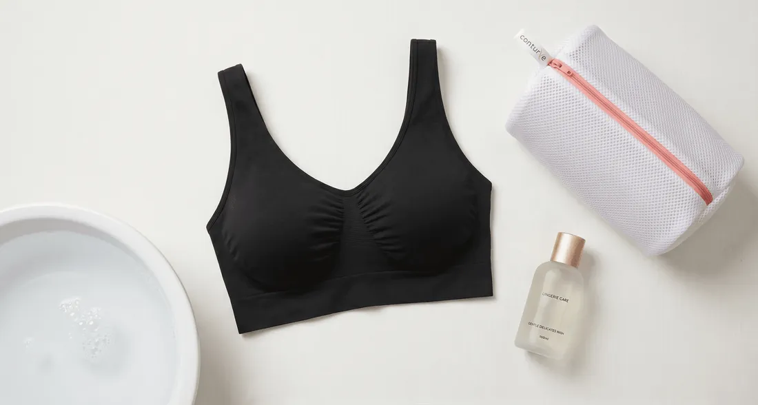 Hands gently washing a delicate bra by hand in a basin of soapy water.